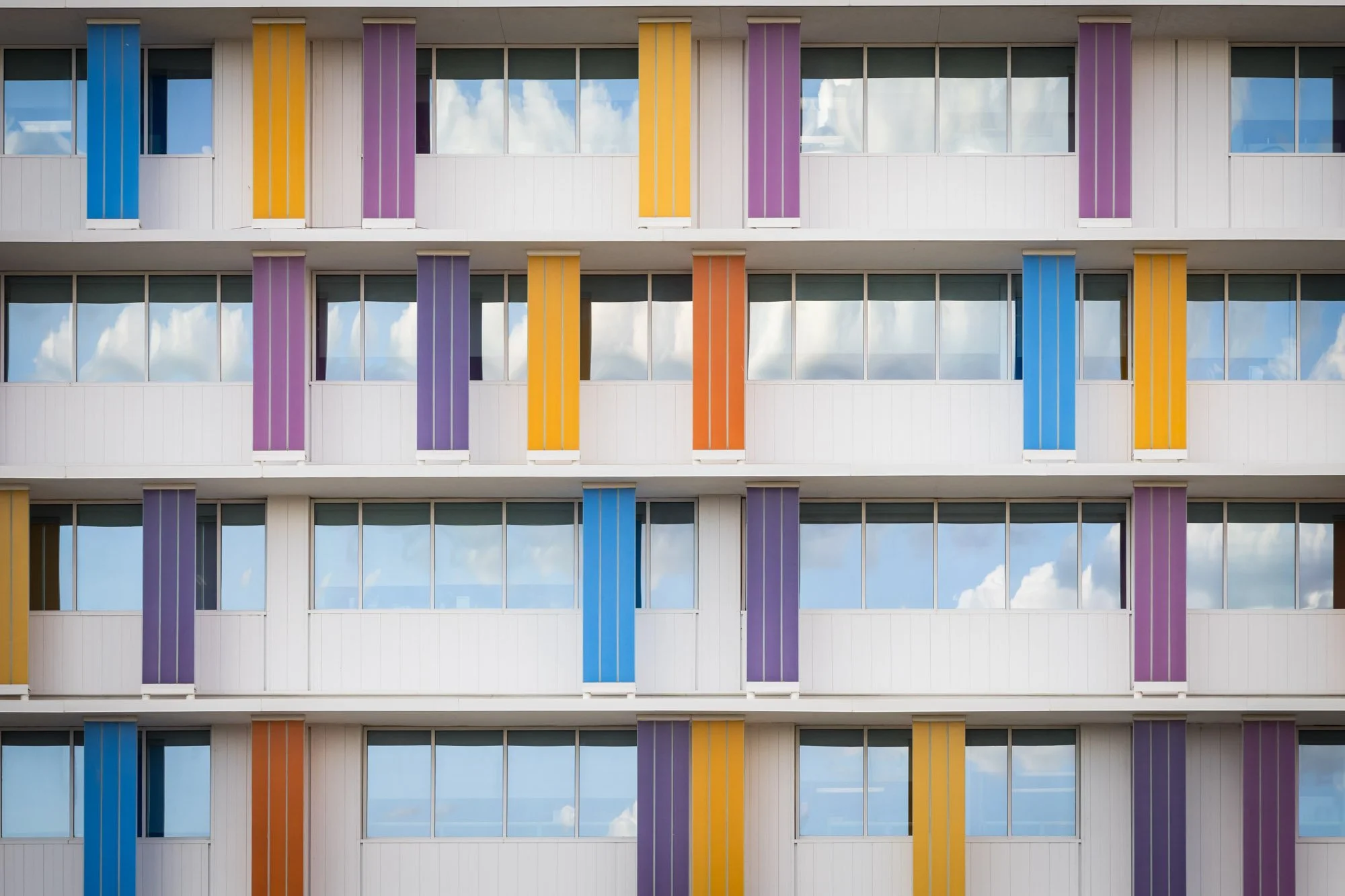 Colorful modern apartment building with white exterior walls, large glass windows, and vertical panels in blue, purple, yellow, and orange.