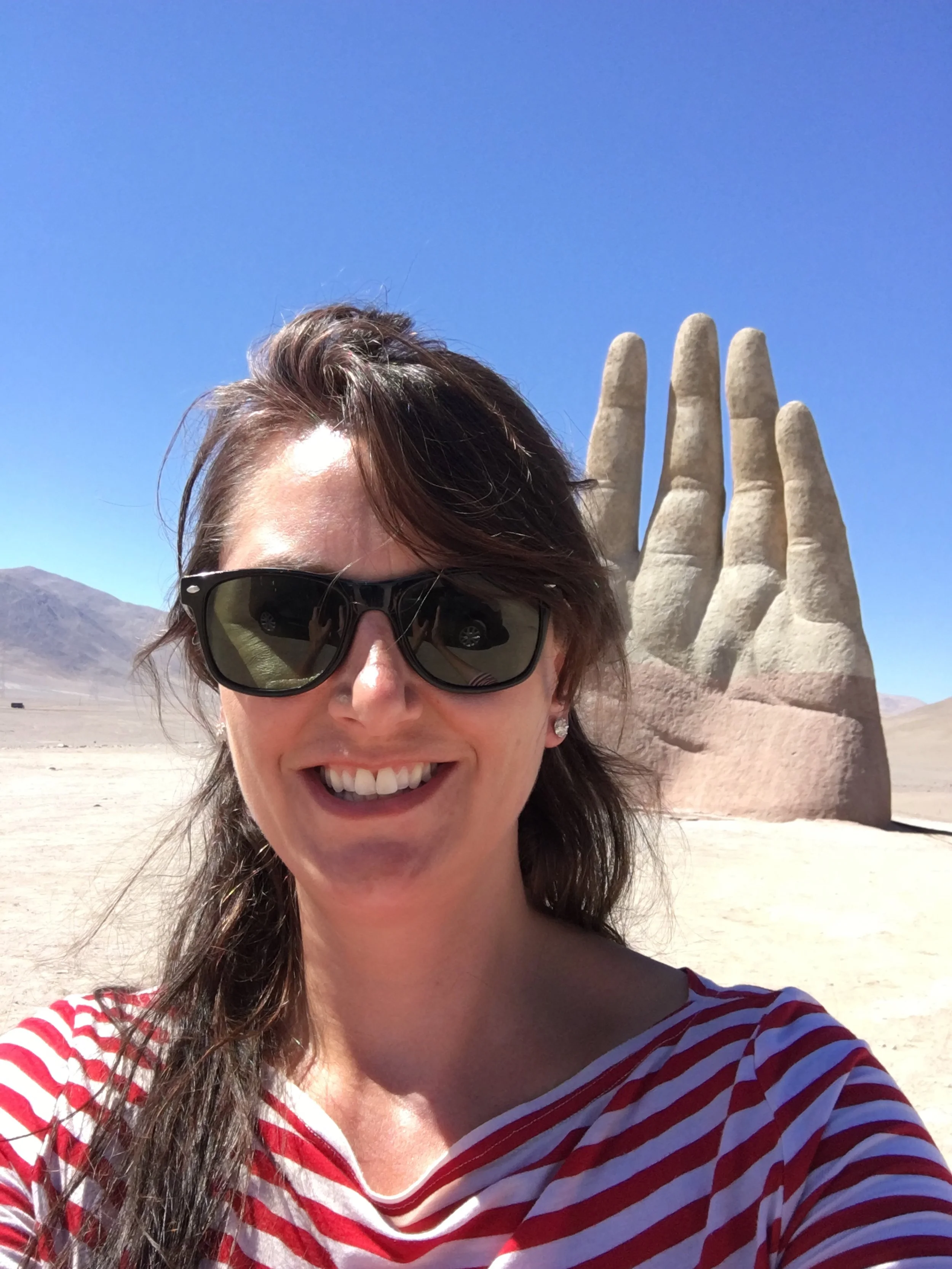 Los Angeles travel photographer and photojournalist, Kelly Williams, wearing sunglasses in front of a stone hand sculpture