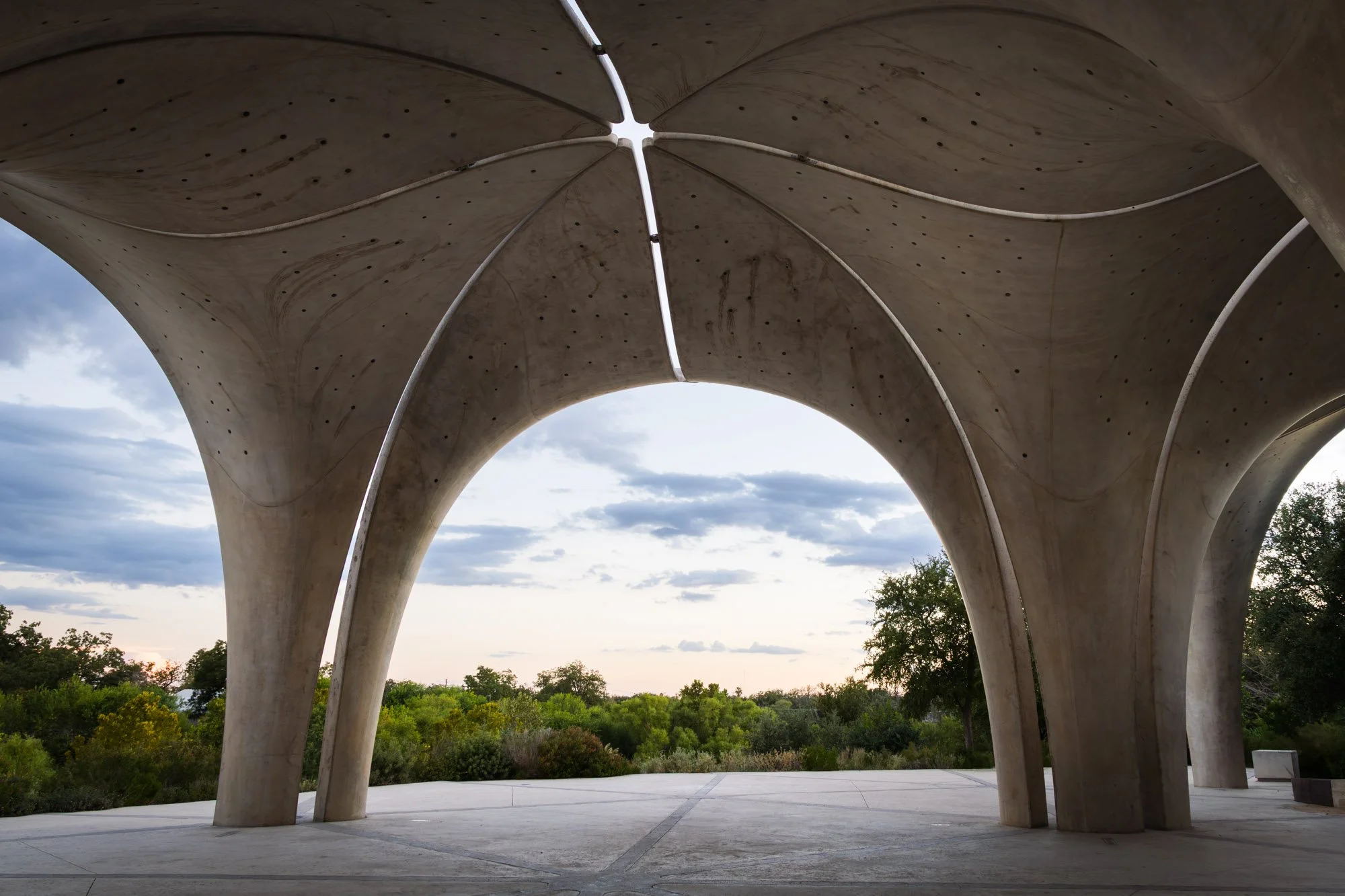 Underneath a large, modern concrete pavilion with curved supports and an open sky in the background.
