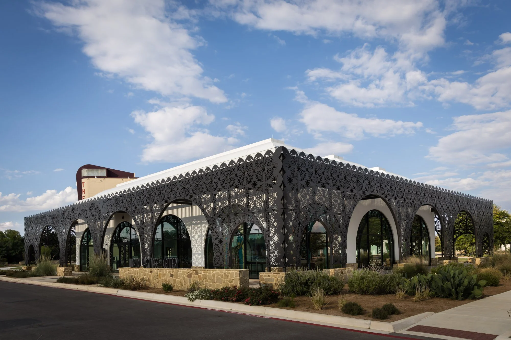 A building with a decorative black metal facade featuring arched windows and desert landscaping in the foreground.