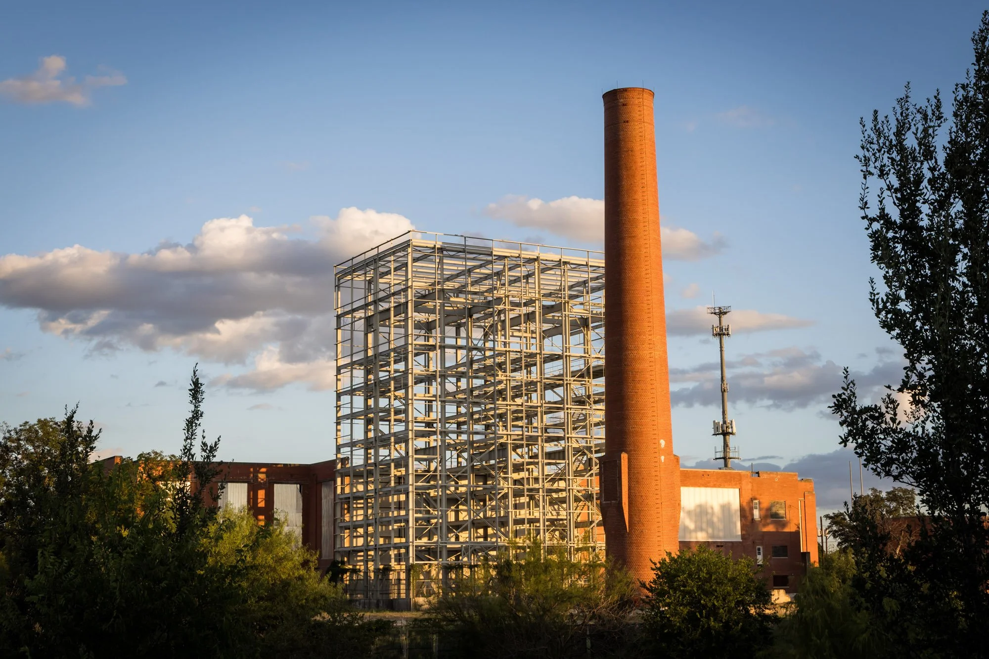 A tall brick chimney next to a steel frame structure on a partly cloudy sky background.