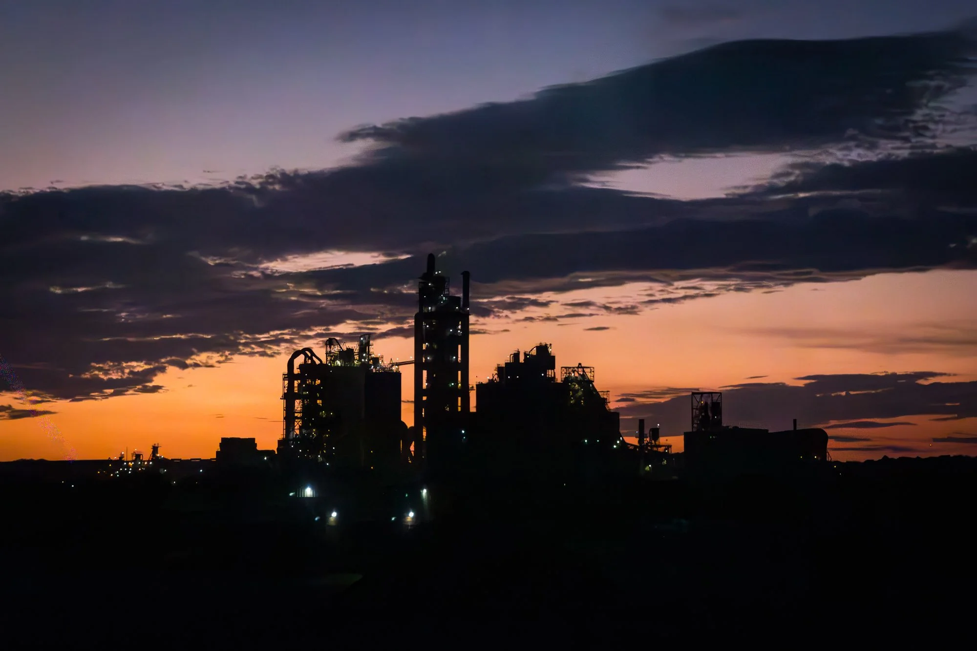 Silhouette of an industrial factory at sunset with colorful sky and dark clouds.