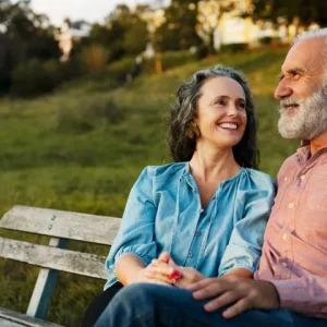 A smiling woman and an older man sitting on a park bench outdoors during daytime.