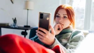 Young woman with red hair taking a selfie with her phone indoors.