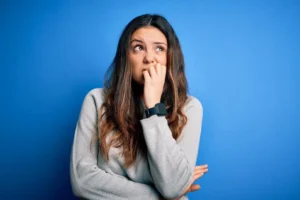 A young woman with long hair looking thoughtful against a blue background.