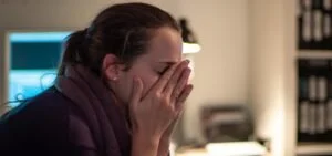 Woman covering her face with her hands, appearing upset or stressed in an office setting.