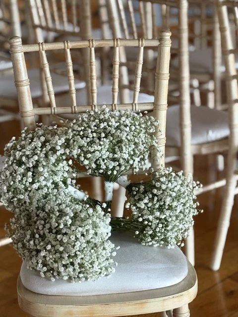 A white chair with a floral arrangement of small white flowers on top, set against a background of more chairs.