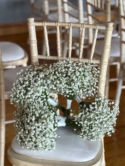 A decorative chair with a large bouquet of baby's breath flowers in front of it, likely arranged for a wedding or special event.