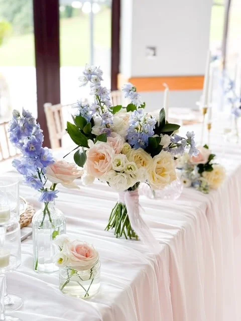Elegant flower centerpiece with white, pink, and blue blooms on a decorated table.
