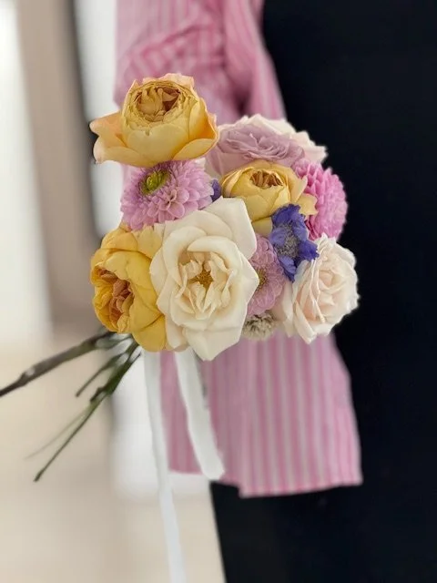 Person holding a bouquet of pastel-colored flowers including yellow, white, pink, and purple blooms.