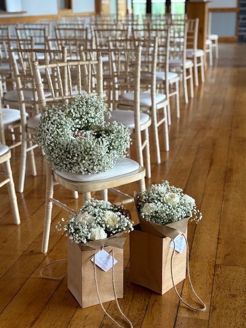 Rows of white chairs arranged for an event with floral decorations and small paper bags at the front.