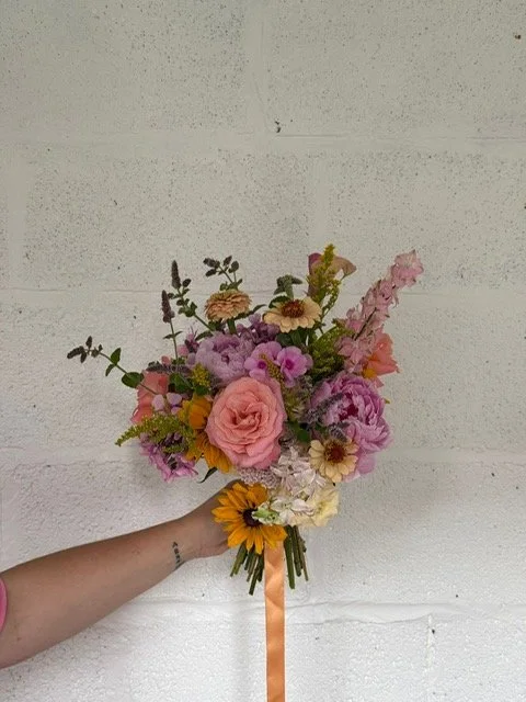Hand holding a colorful bouquet of flowers against a white wall