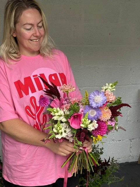 Woman in a pink t-shirt holding a colorful bouquet of flowers.