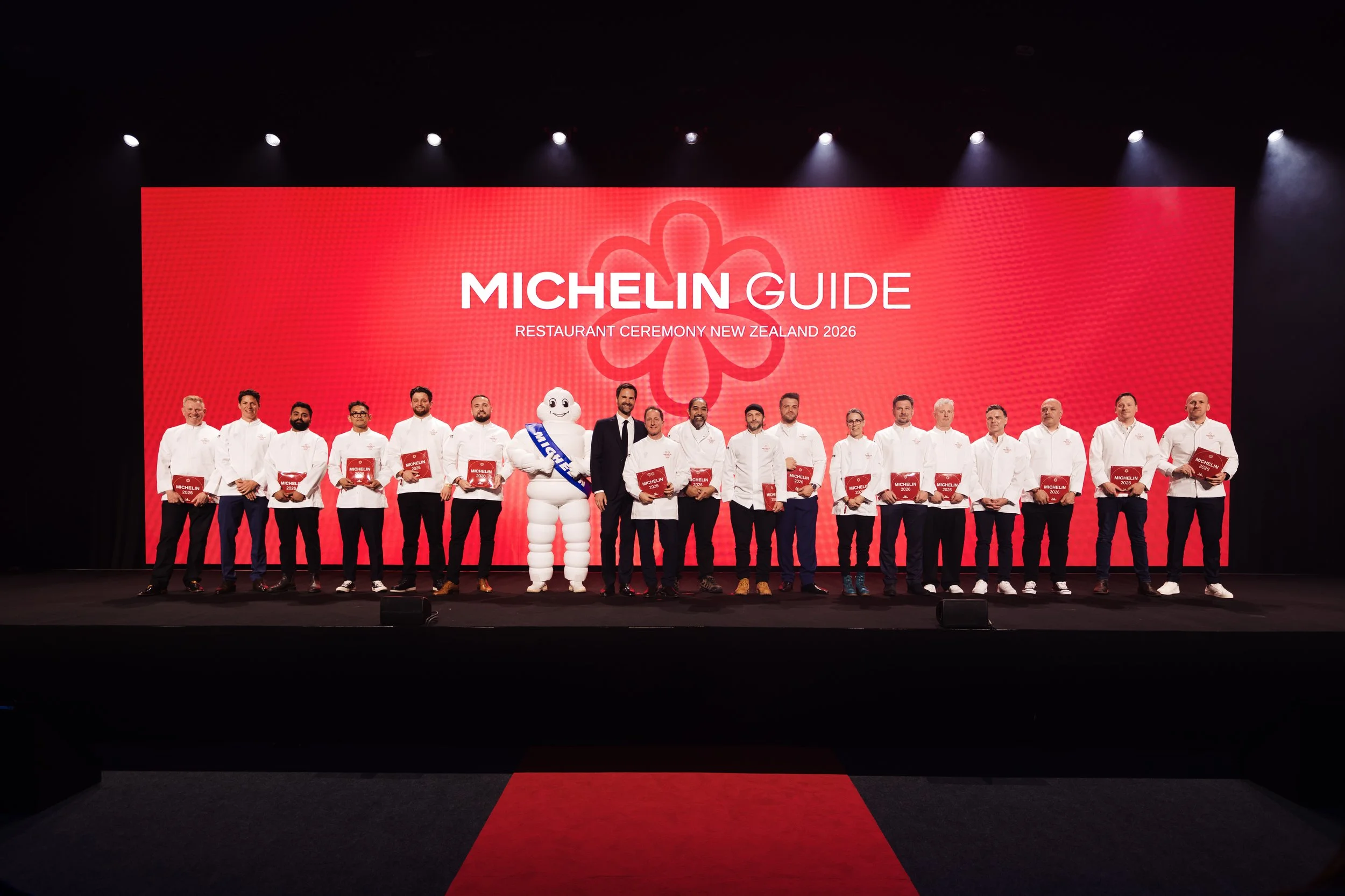 A group of chefs and officials on stage holding Michelin guide award plaques during a ceremony with a large red background displaying 'Michelin Guide' and 'Restaurant Ceremony New Zealand 2026'.