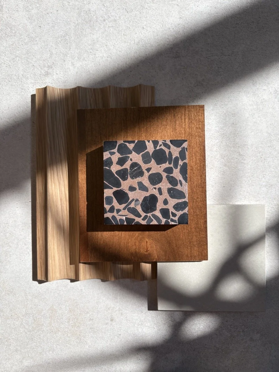 Top-down view of a wooden table with terrazzo-style tile, wooden book and choo-choo train patterned paper on a white surface, with shadows cast across the scene.