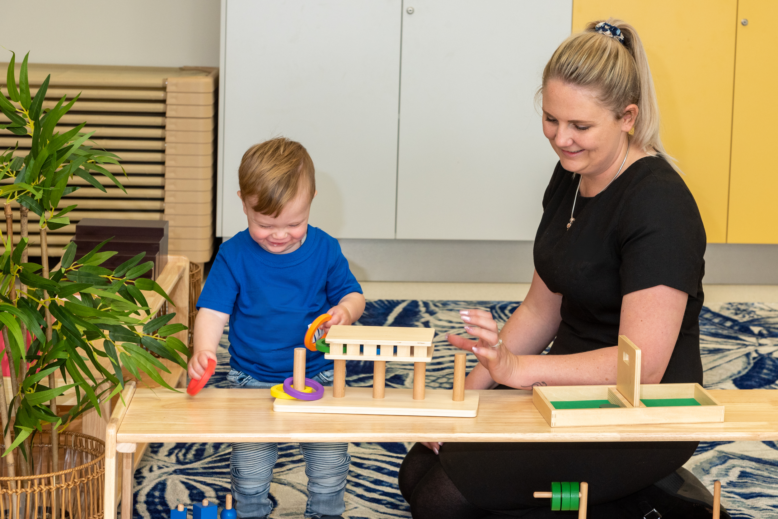 Child practices placing coloured rings on pegs with the help of an Educator