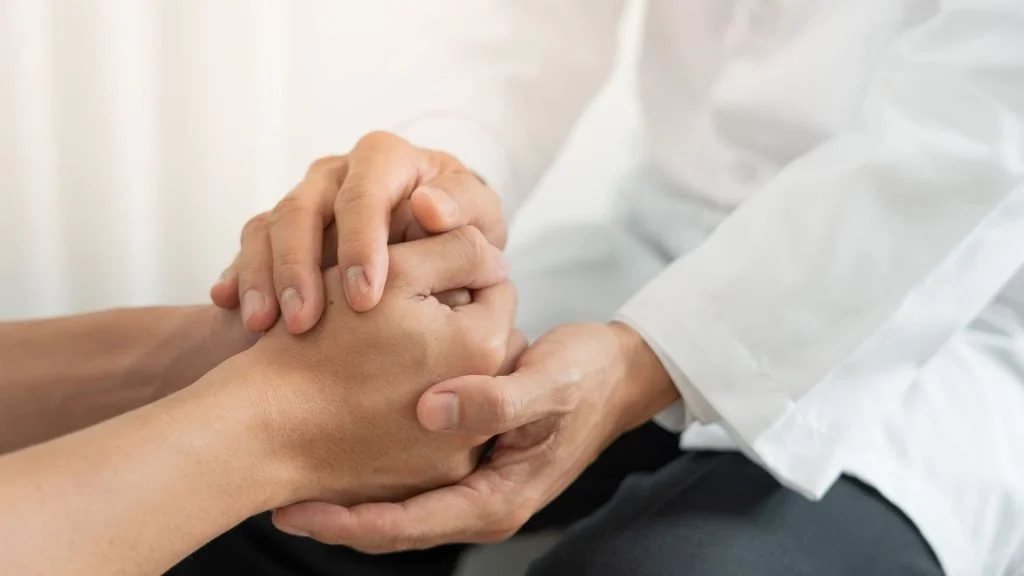 A person in a white shirt holding and comforting someone with their hands clasped together