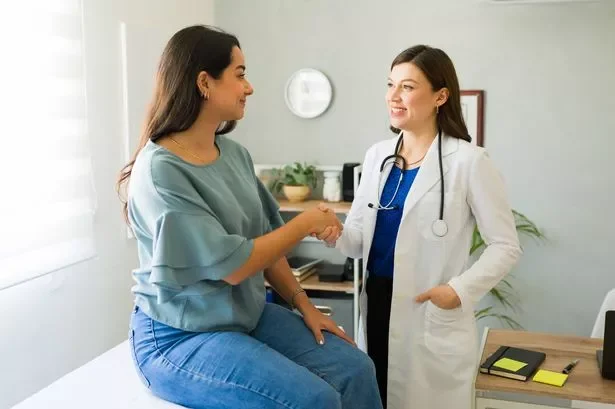 A female doctor and a pregnant woman shaking hands in a medical examination room.