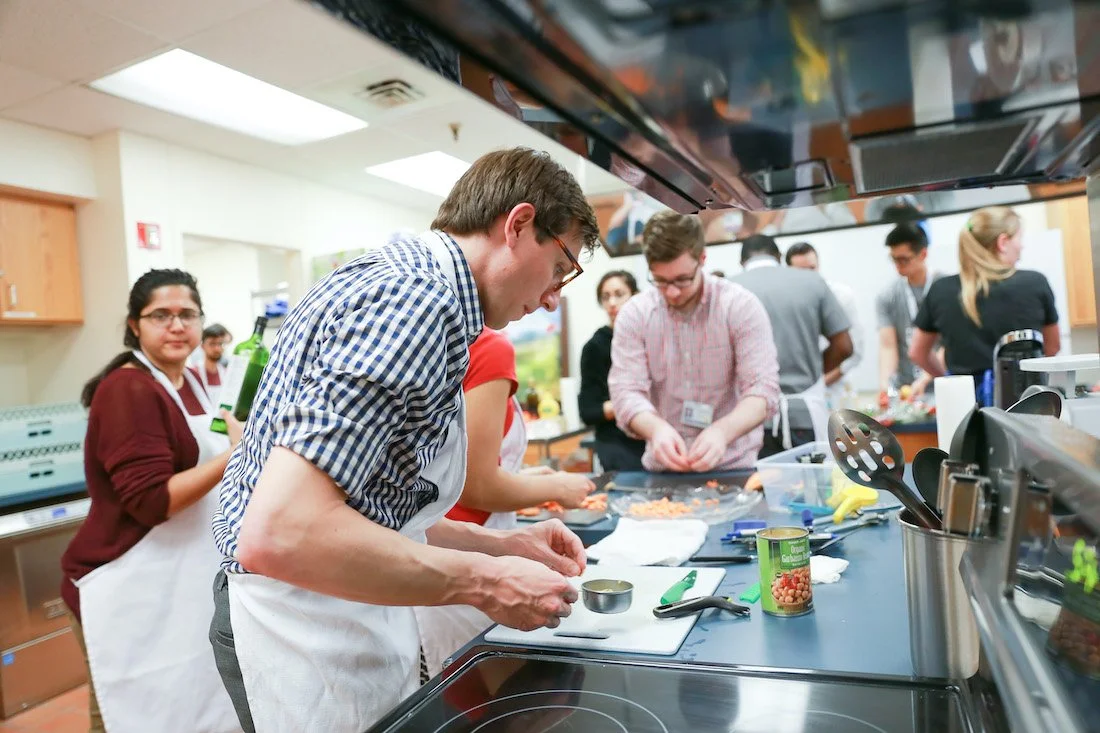 People cooking together in a kitchen, wearing aprons and preparing food.