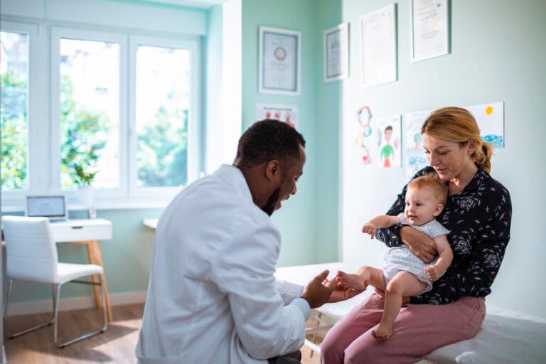 A healthcare professional speaking with a mother while holding her baby in a clinic or doctor's office.