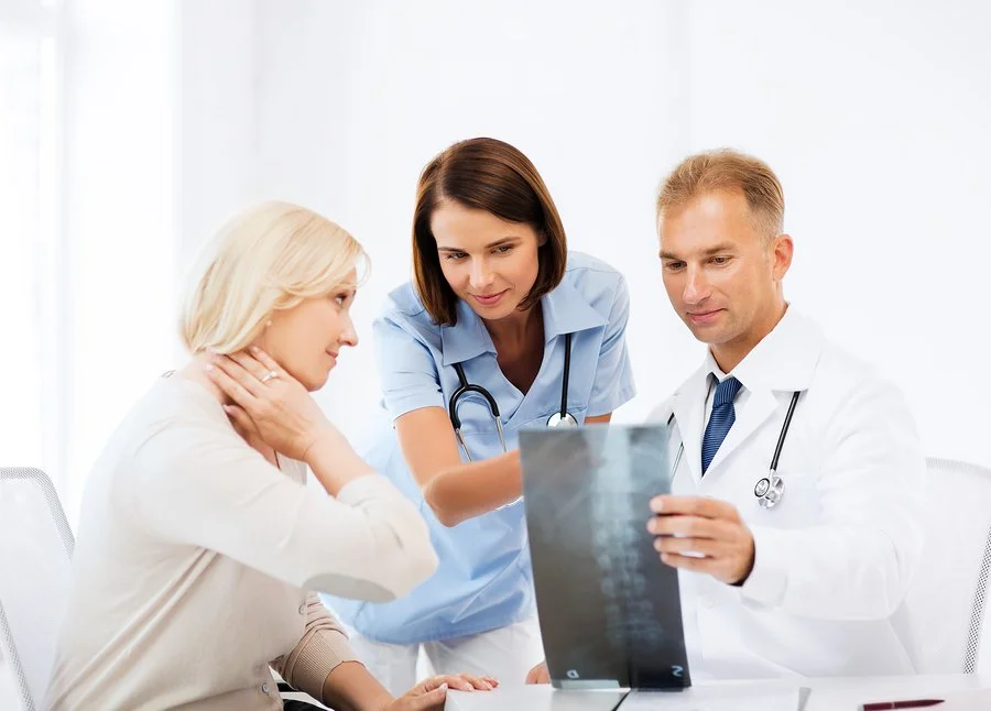 Three healthcare professionals, including a female nurse and two doctors, examine an x-ray film together in a well-lit clinical setting.