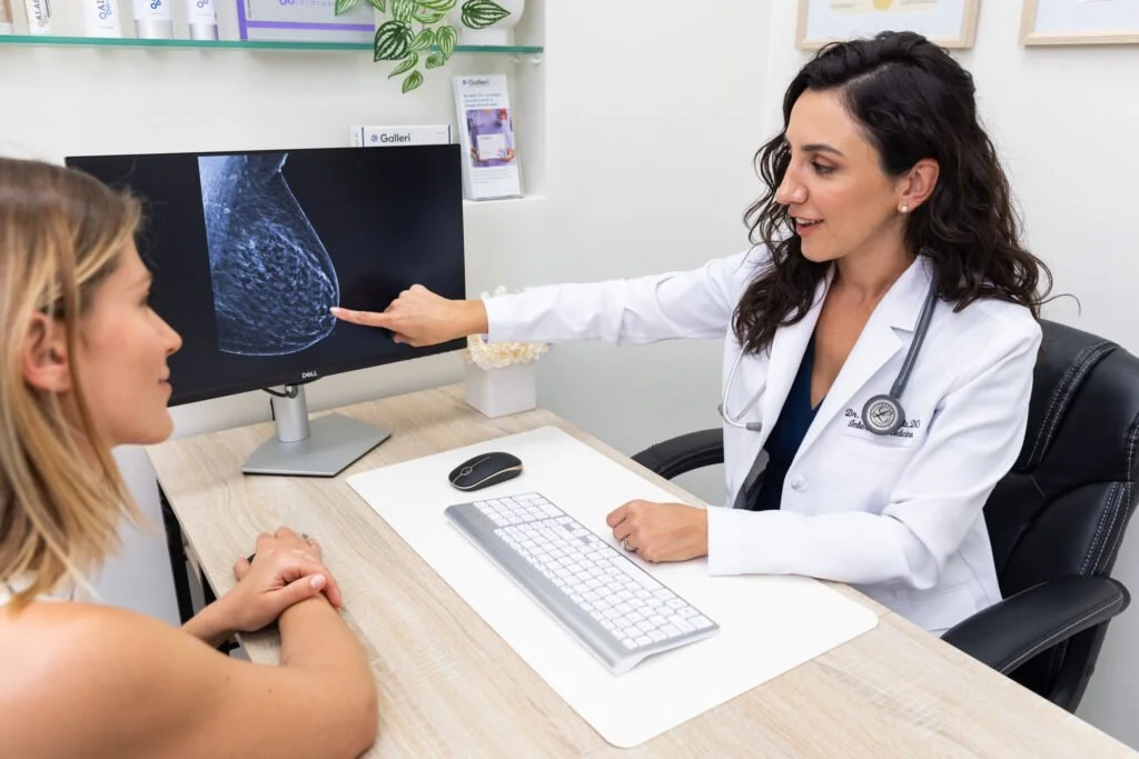 A female doctor explaining a mammogram image to a female patient in an office setting.