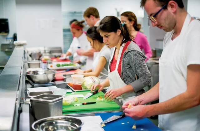 People in a cooking class chopping vegetables at a long counter.
