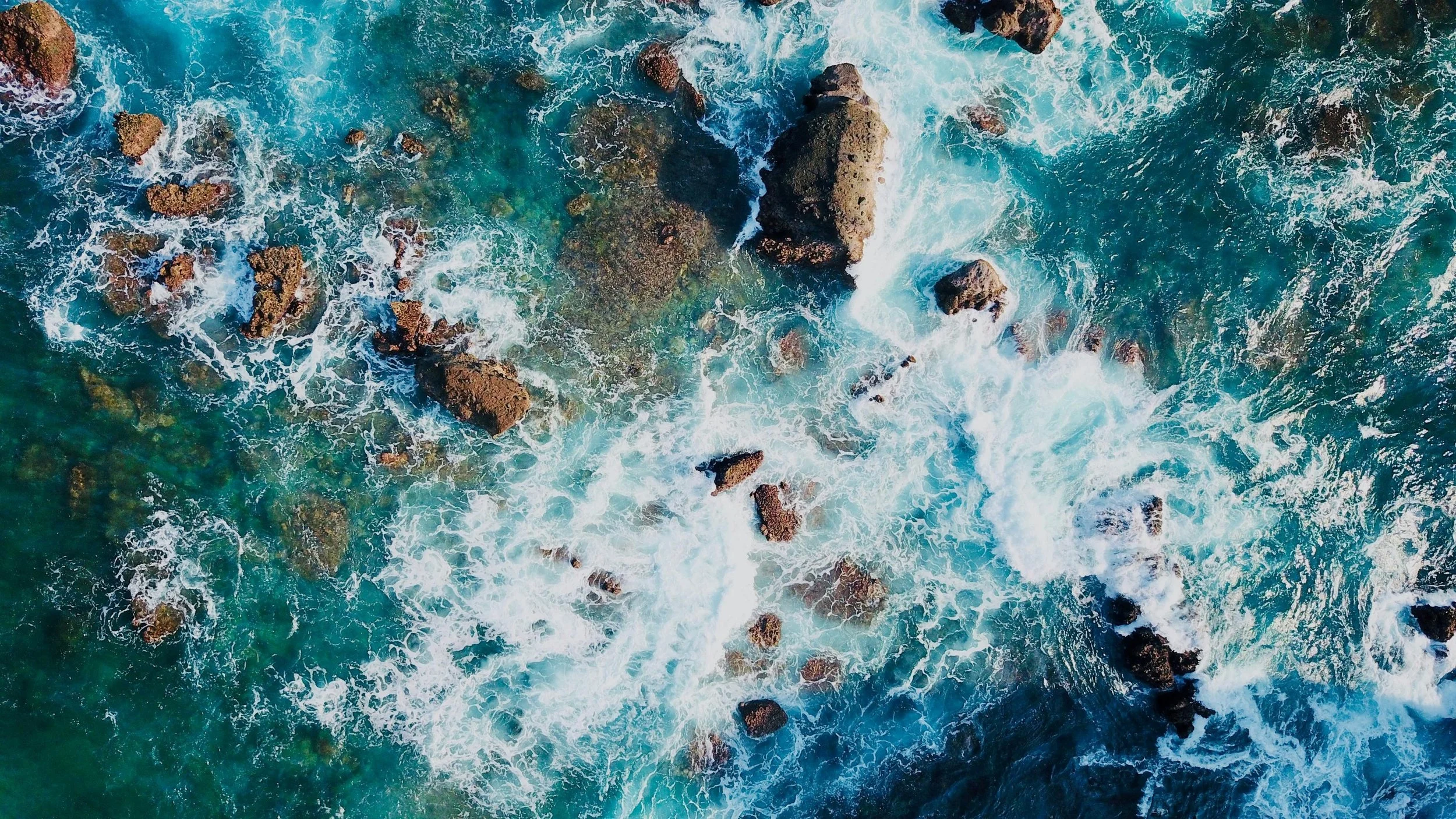 Aerial view of ocean waves crashing over rocks in sea water.