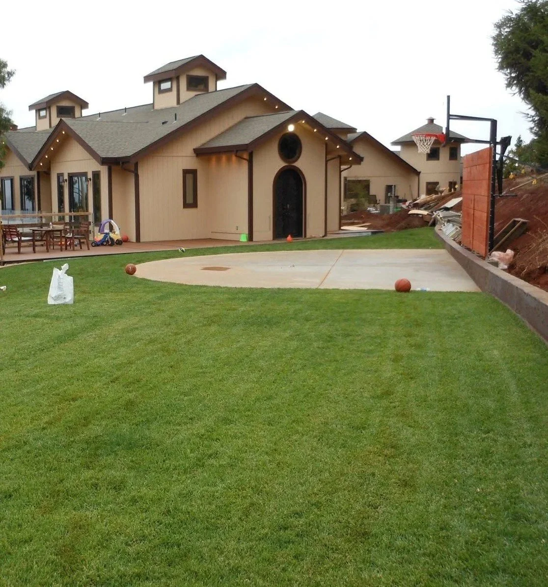 Large house with a backyard basketball court and a grassy lawn, with some construction work visible on the side.