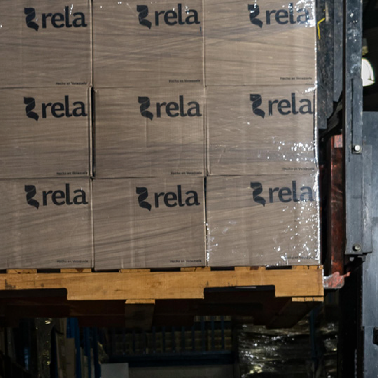 Stack of cardboard boxes with 'rela' printed on them, stored on a wooden pallet in a warehouse.