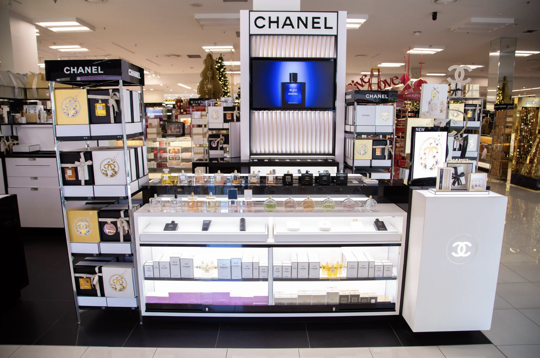 Display of Chanel perfumes and cosmetics in a retail store, with a large Chanel logo and branding, surrounded by shelves of products and decorative items.