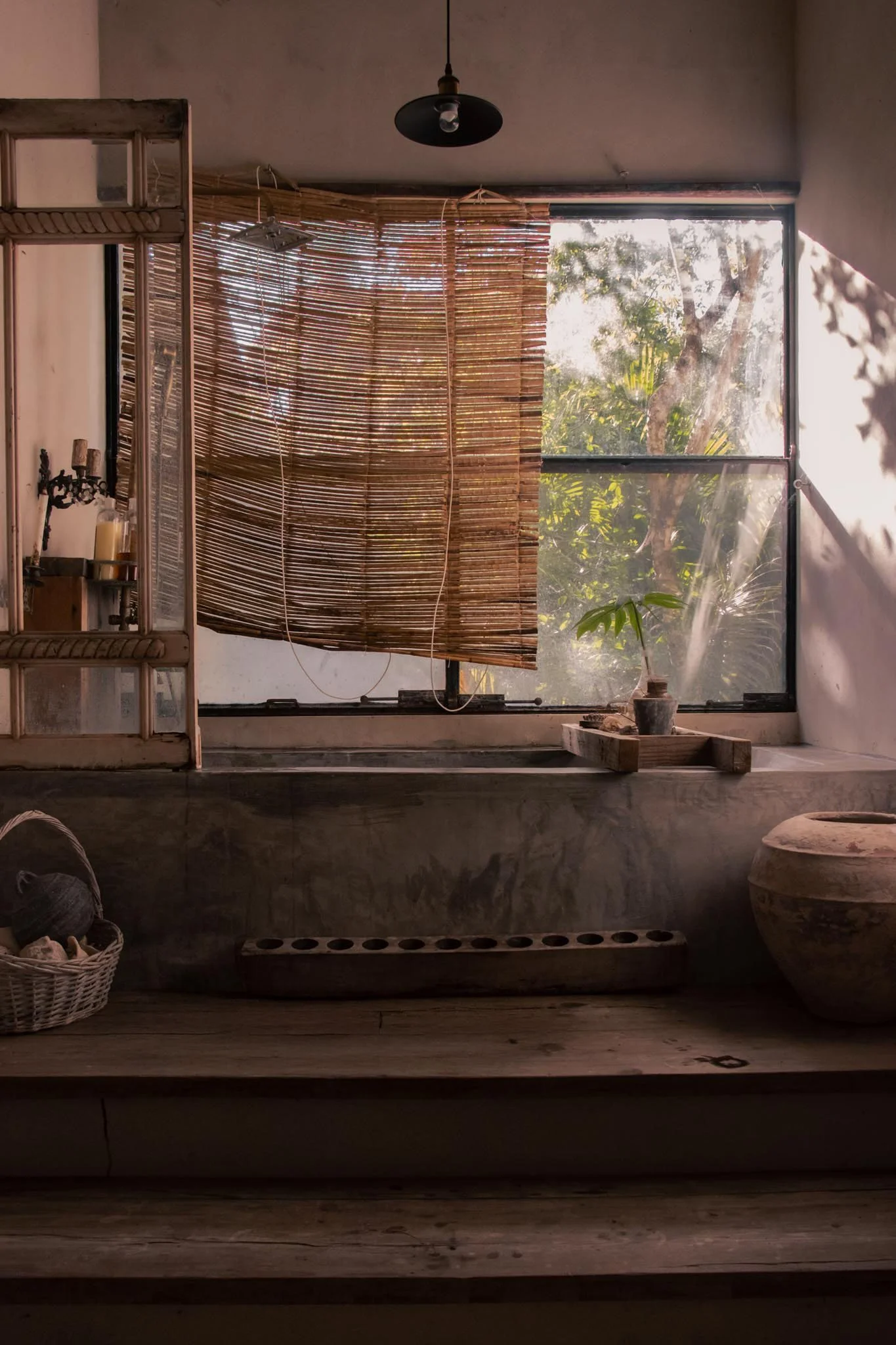 Fotografía de Interior de una bañera con ventana grande y cortina de troncos de madera. El estilo y decoración es ecléctico y rústico con esencia selvática, pues la casa se encuentra en medio de la selva de Quintana Roo.