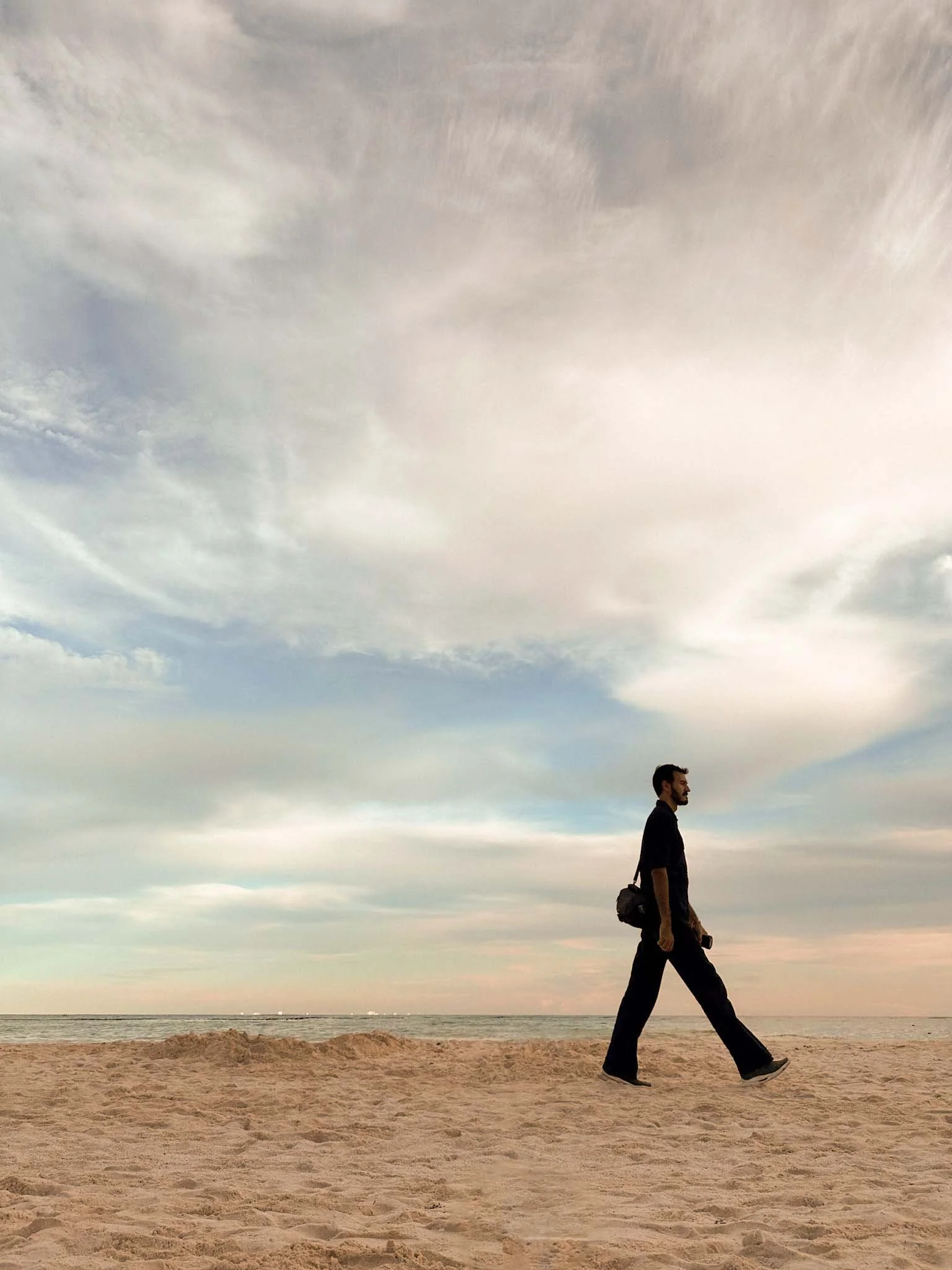 Hombre caminando por la arena de la playa con , cielo del atardecer, nublado brillante. Ambiente tranquilo.