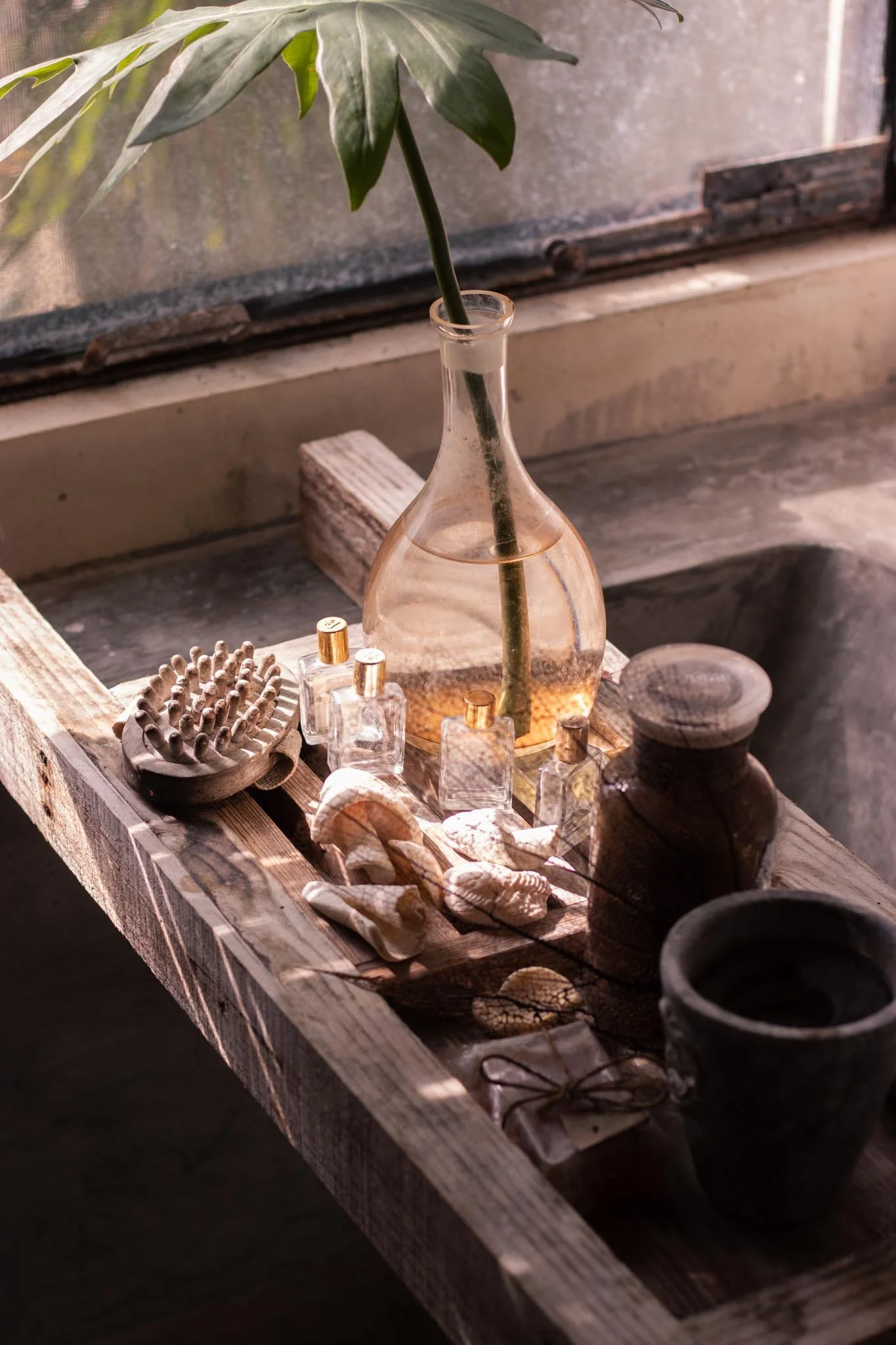 Fotografía del decoración de interior natural, con botellas de vidrio, conchas, pequeños frascos de perfume y otros objetos en una mesa de madera junto a una gran ventana que ilumina las escena de manera natural.