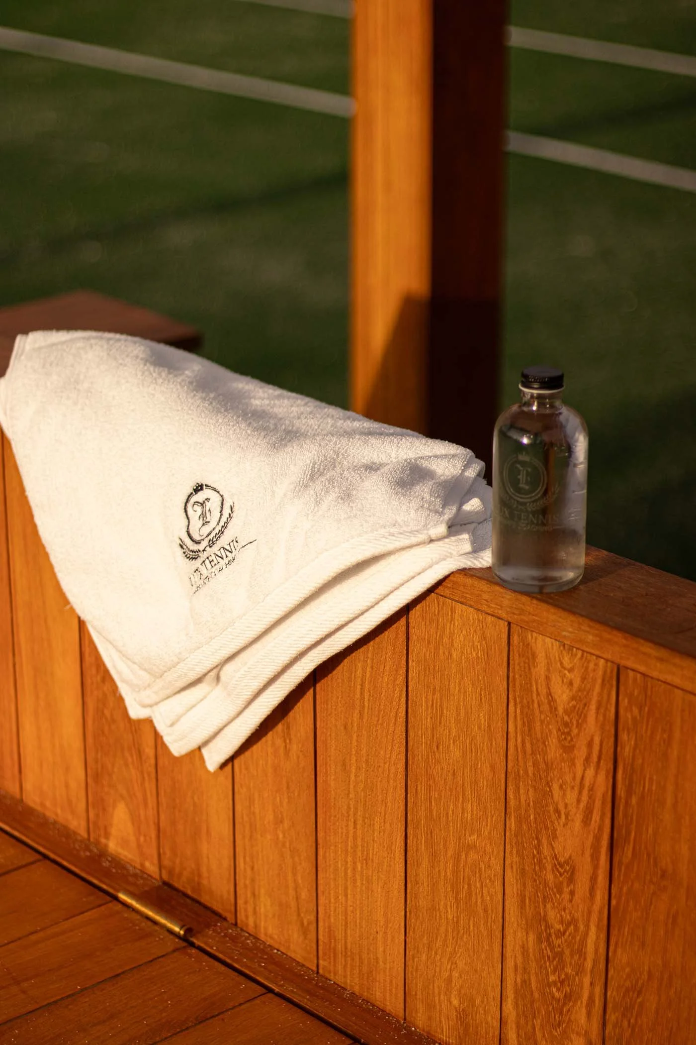 Fotografía publicitaria para canchas de tenis, se ve una toalla blanca y una botella de agua con la marca de la empresa.
