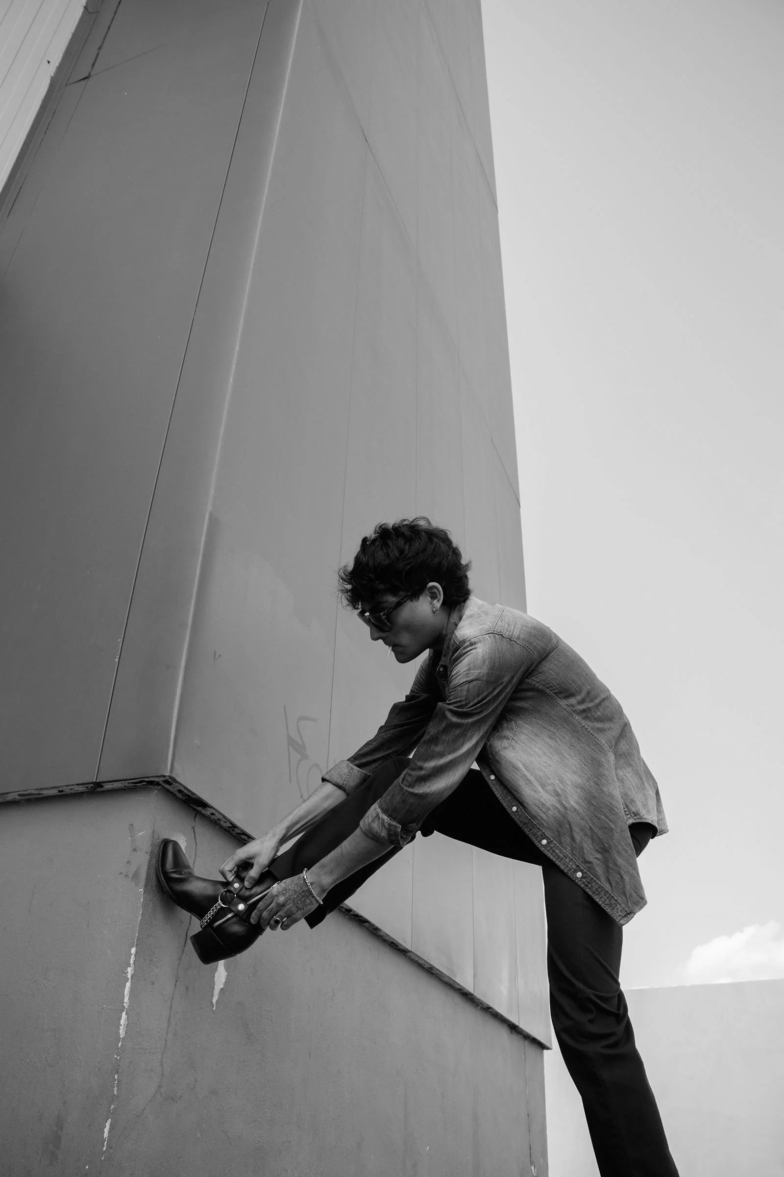 Fotografía editorial en blanco y neegro de modelo masculino en un entorno urbano y geométrico, con cielo despejado.