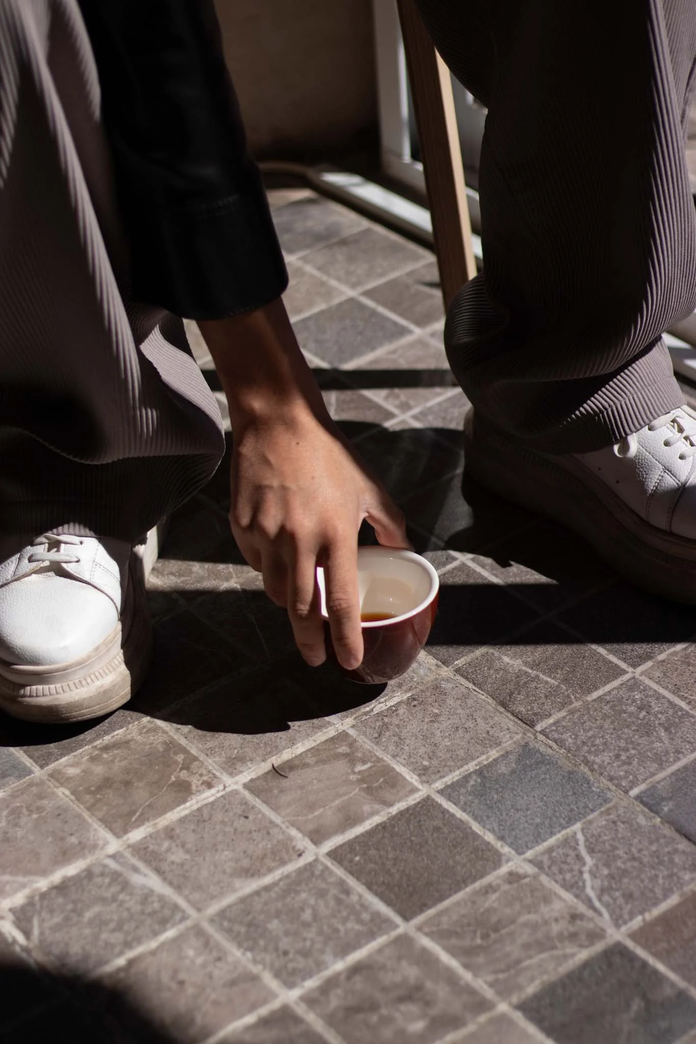 Fotografía de estilo de vida, iluminada con luz natural que dibuja siluetas. Se ve una mano levantando una taza con café.