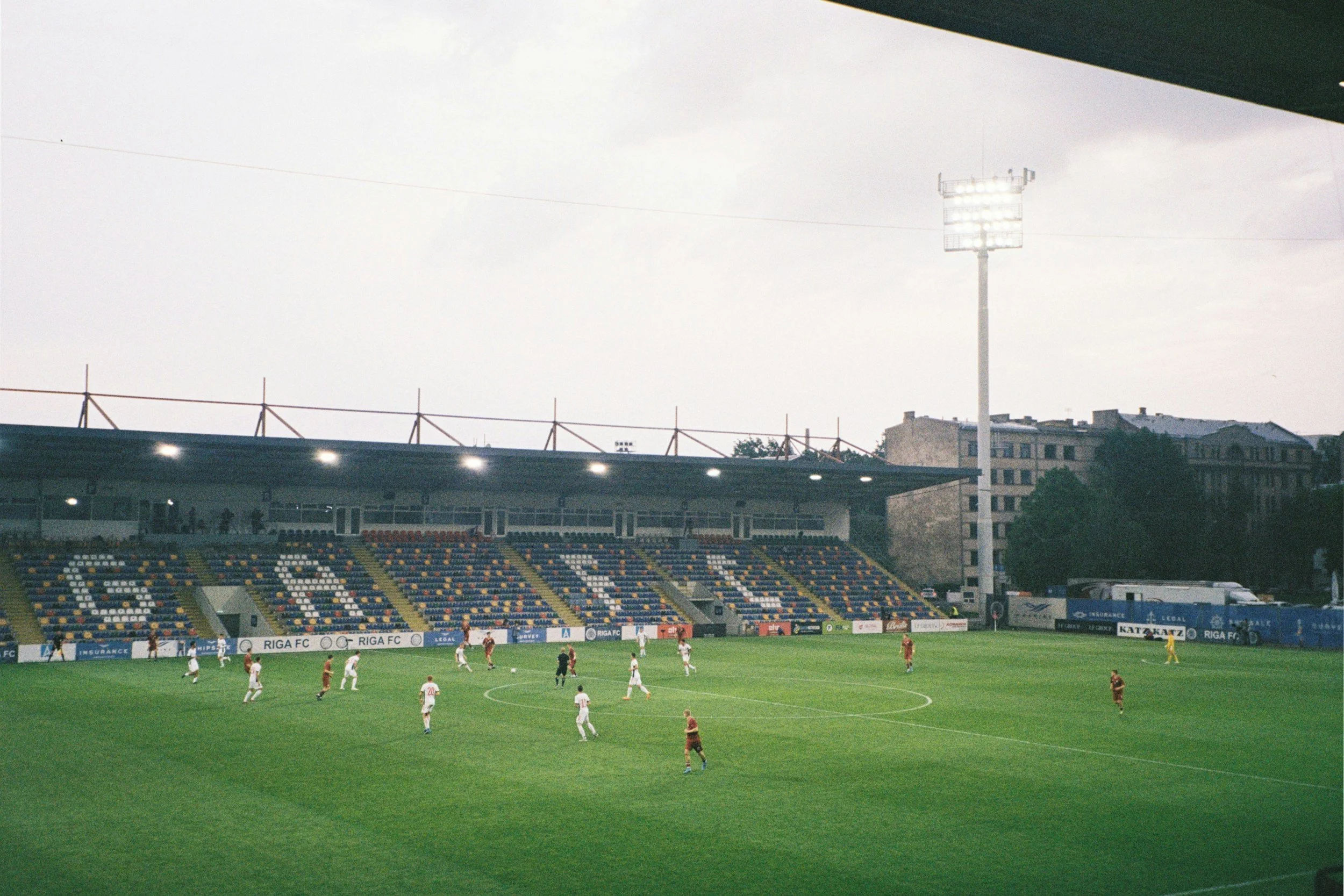 Soccer match in a stadium, players on the field, with the stadium's stands and advertising banners visible in the background.