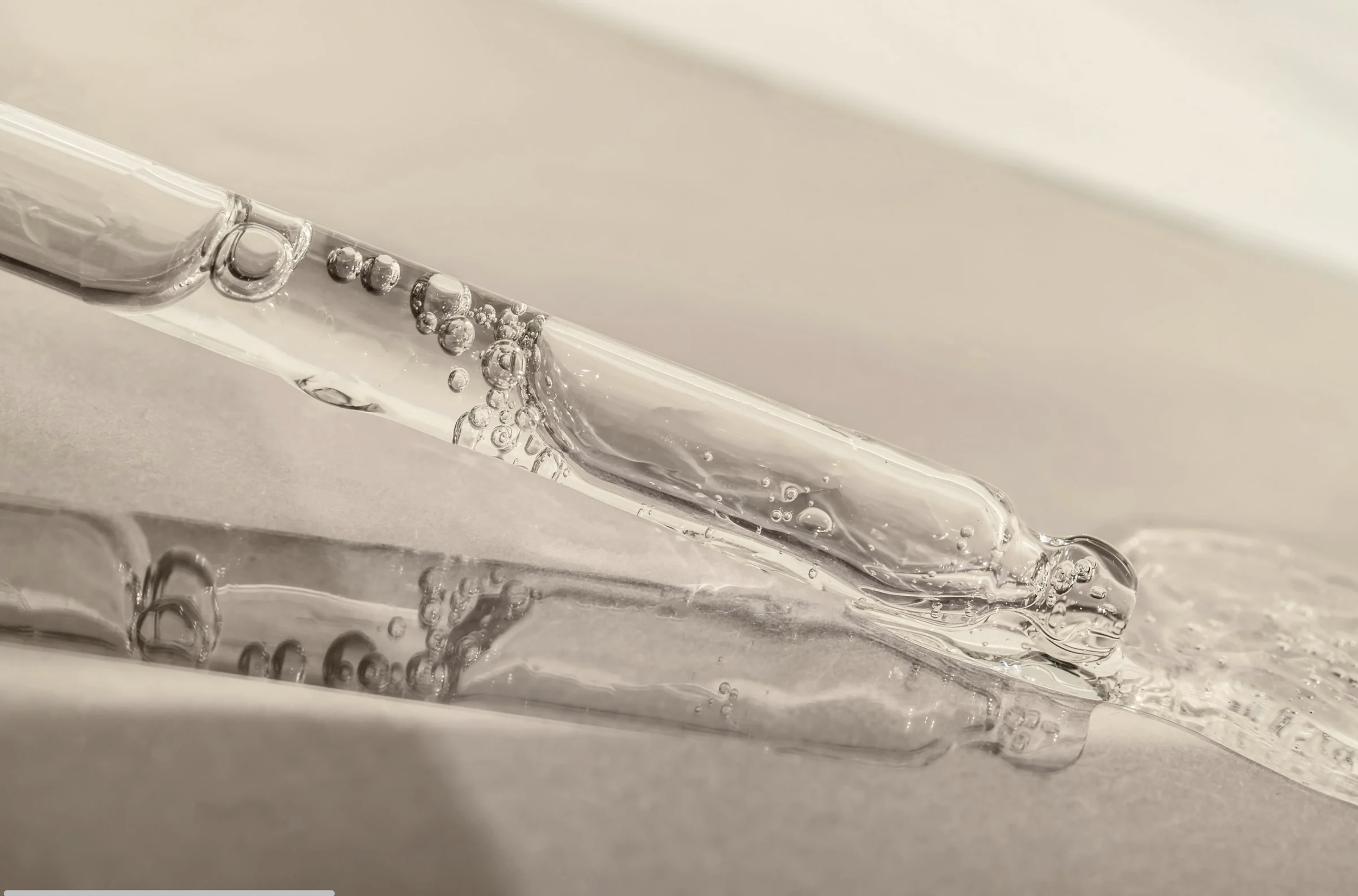 Close-up of a glass test tube filled with a clear liquid, with bubbles rising inside, resting on a flat surface.
