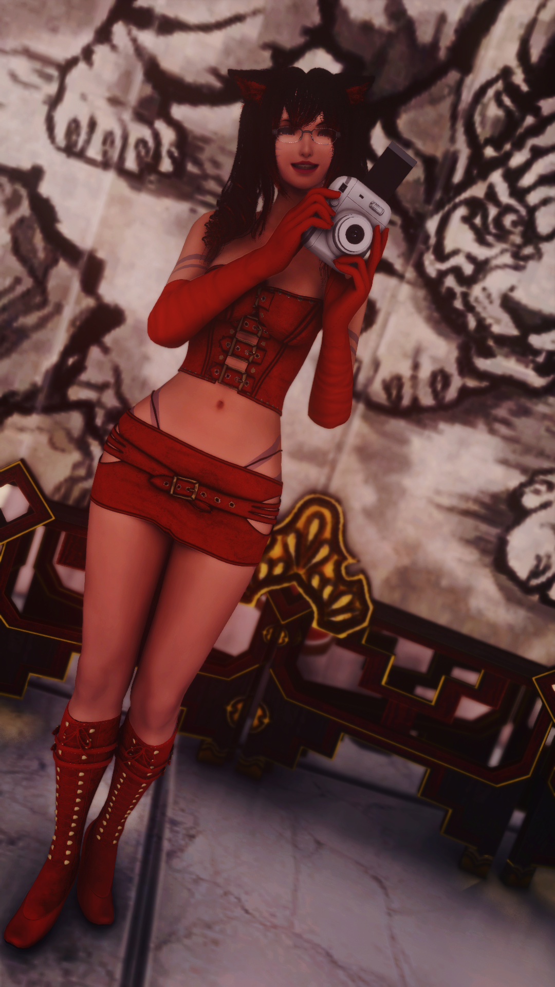 A woman dressed in a red corset and mini skirt with long red gloves and red high boots standing in front of a decorative wall and taking a selfie with a camera. She has black hair, glasses, and cat ears.