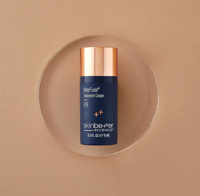 A bottle of Skinbetter Science InterFuse Treatment Cream for eyes with a gold cap on a neutral background.