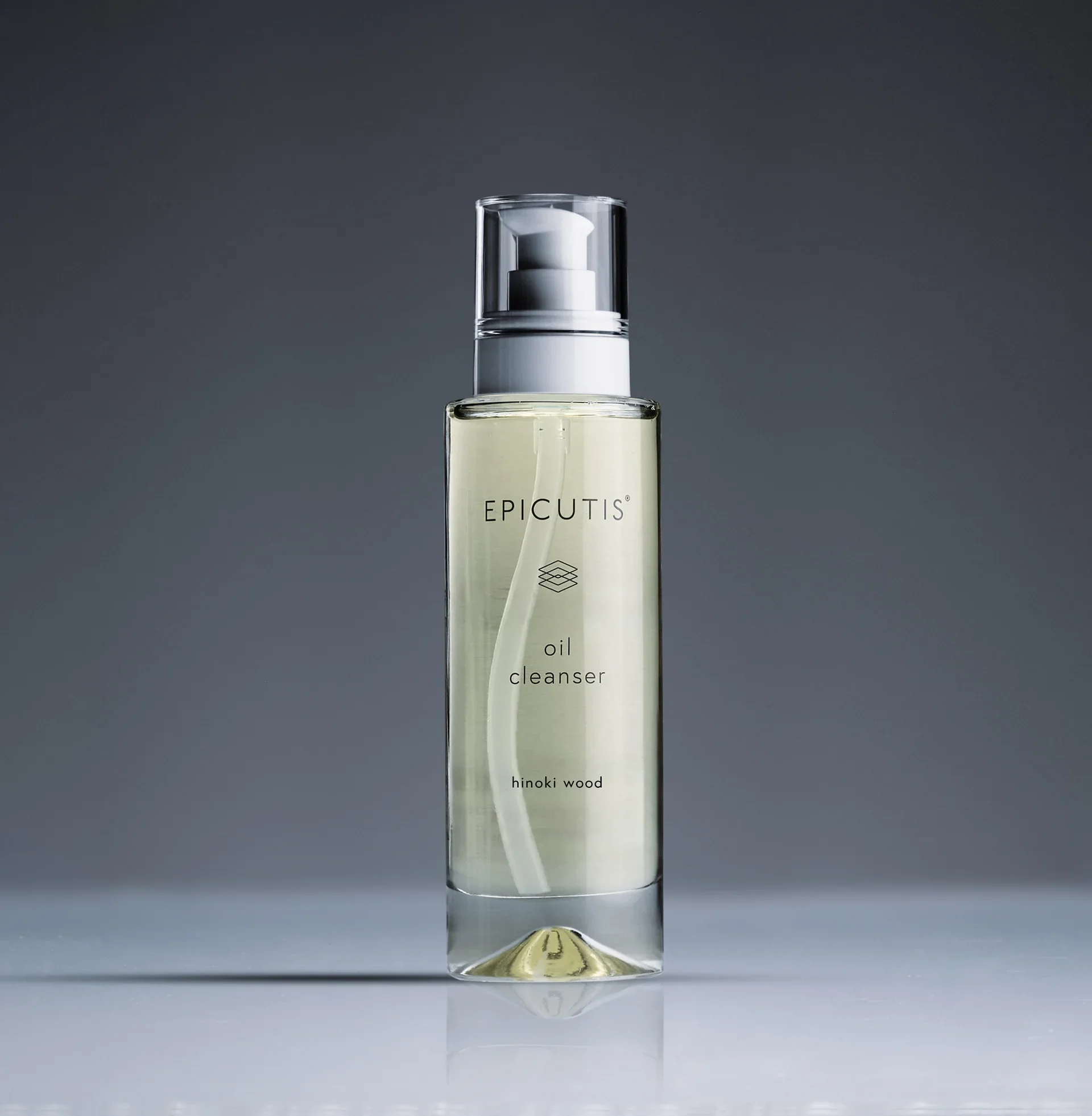 A clear bottle of Epicuts oil cleanser with a pump dispenser, containing yellowish liquid, placed on a reflective surface against a gray background.