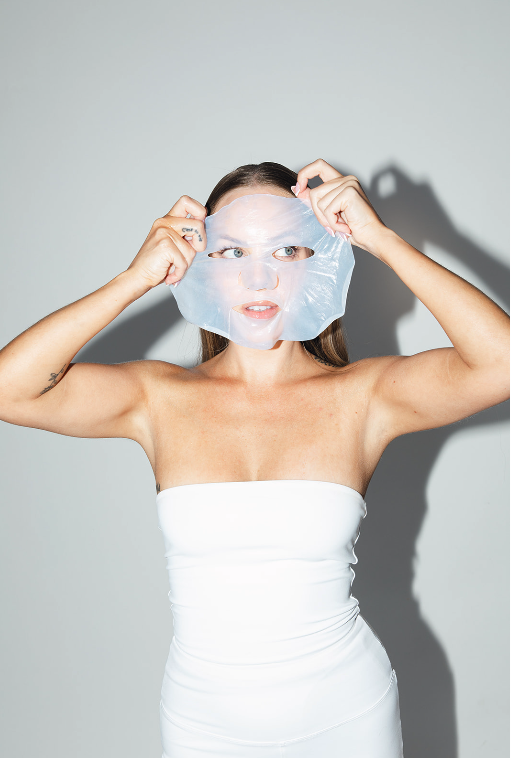 Woman in a white strapless top puts on a translucent face mask.