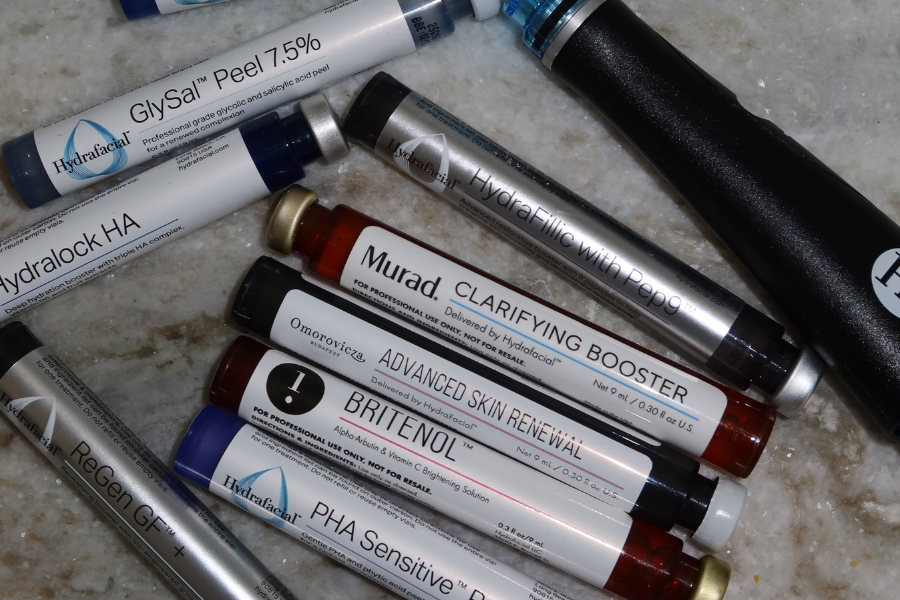 Assorted skincare products, including GlySal peel, Hydralock HA, Murad clarifying booster, Advanced Skin Renewal, BriteNL, PHA Sensitive, and Regen GF+ on a marble surface.