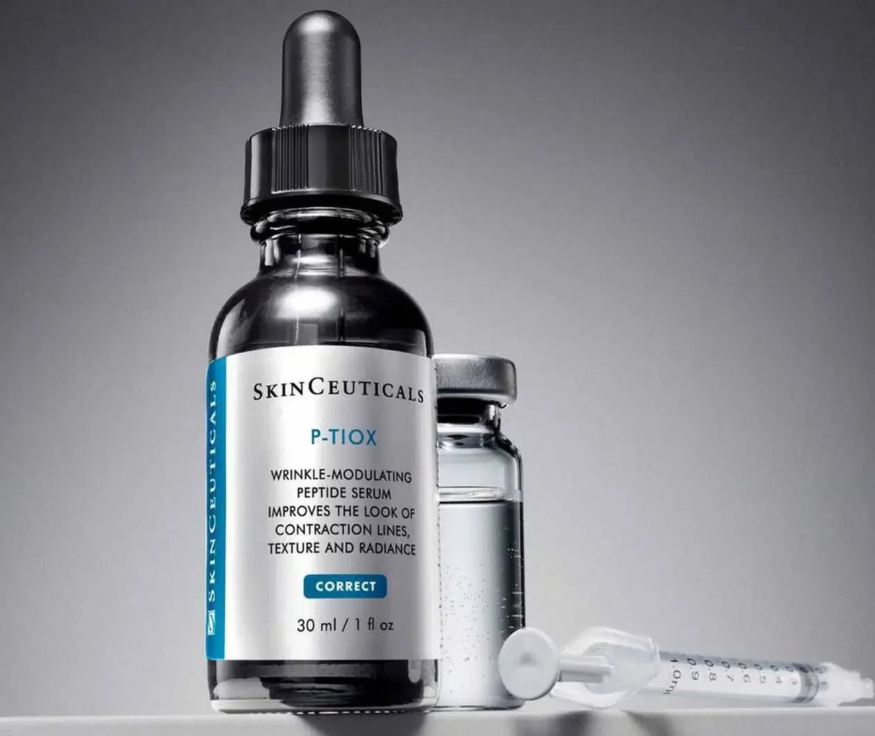 A bottle of SkinCeuticals P-TIX wrinkle-modulating peptide serum with a dropper on top, a small jar behind it, and a syringe lying in front on a gray background.