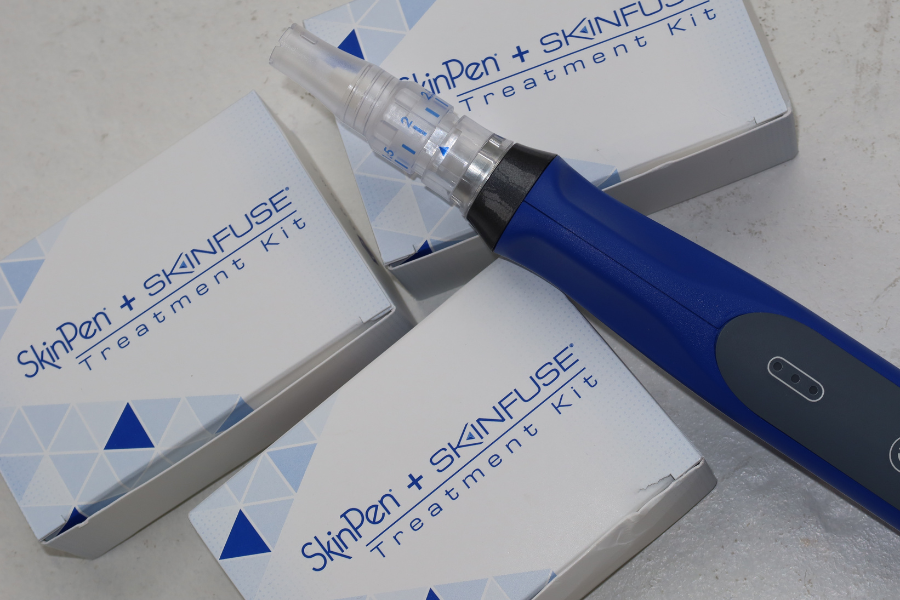 A blue and black dermaplaning tool resting on three boxes labeled 'SkinPen + SKINFUSE Treatment Kit'.