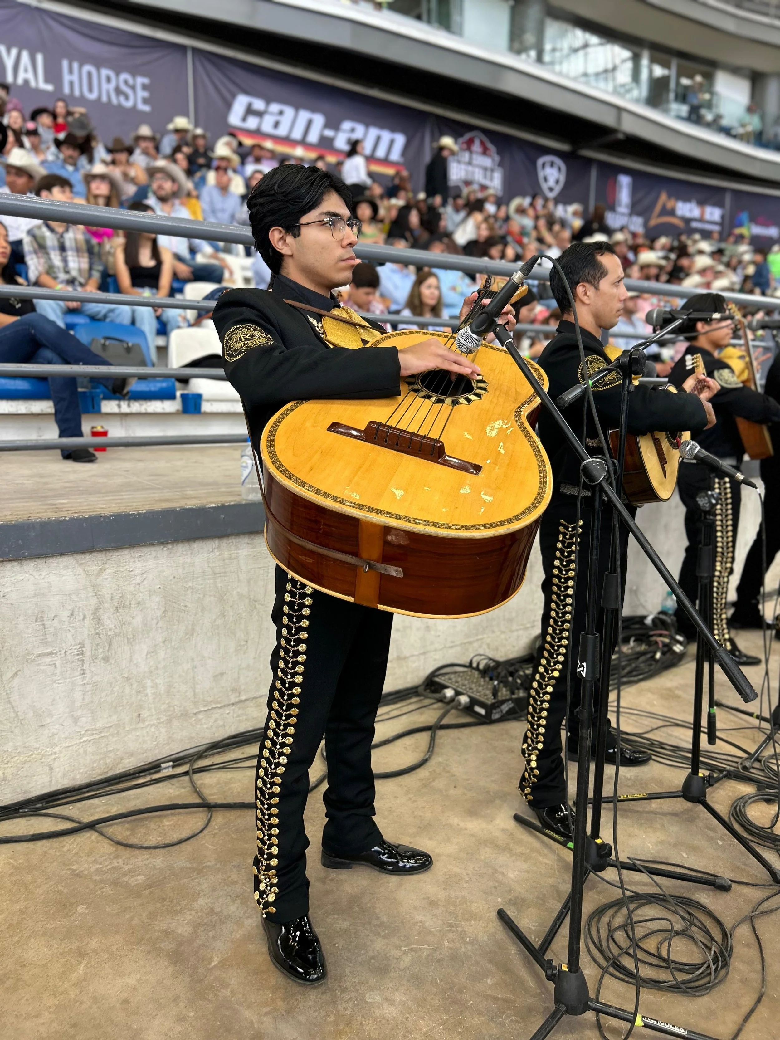 Grupo de músicos tocando guitarra en un evento con audiencia numerosa en el fondo.
