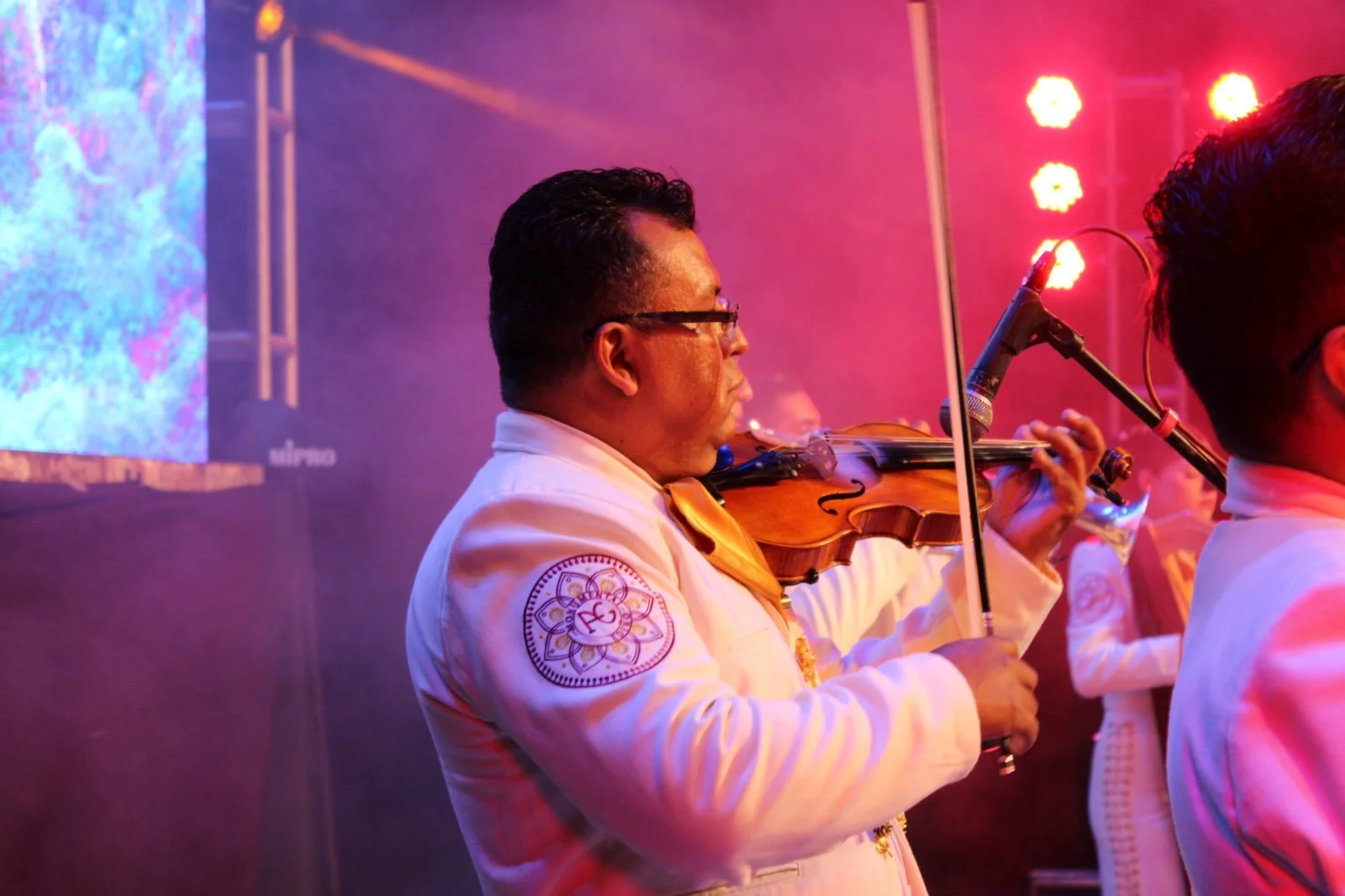Músico tocando violín en un escenario con iluminación roja y morada.