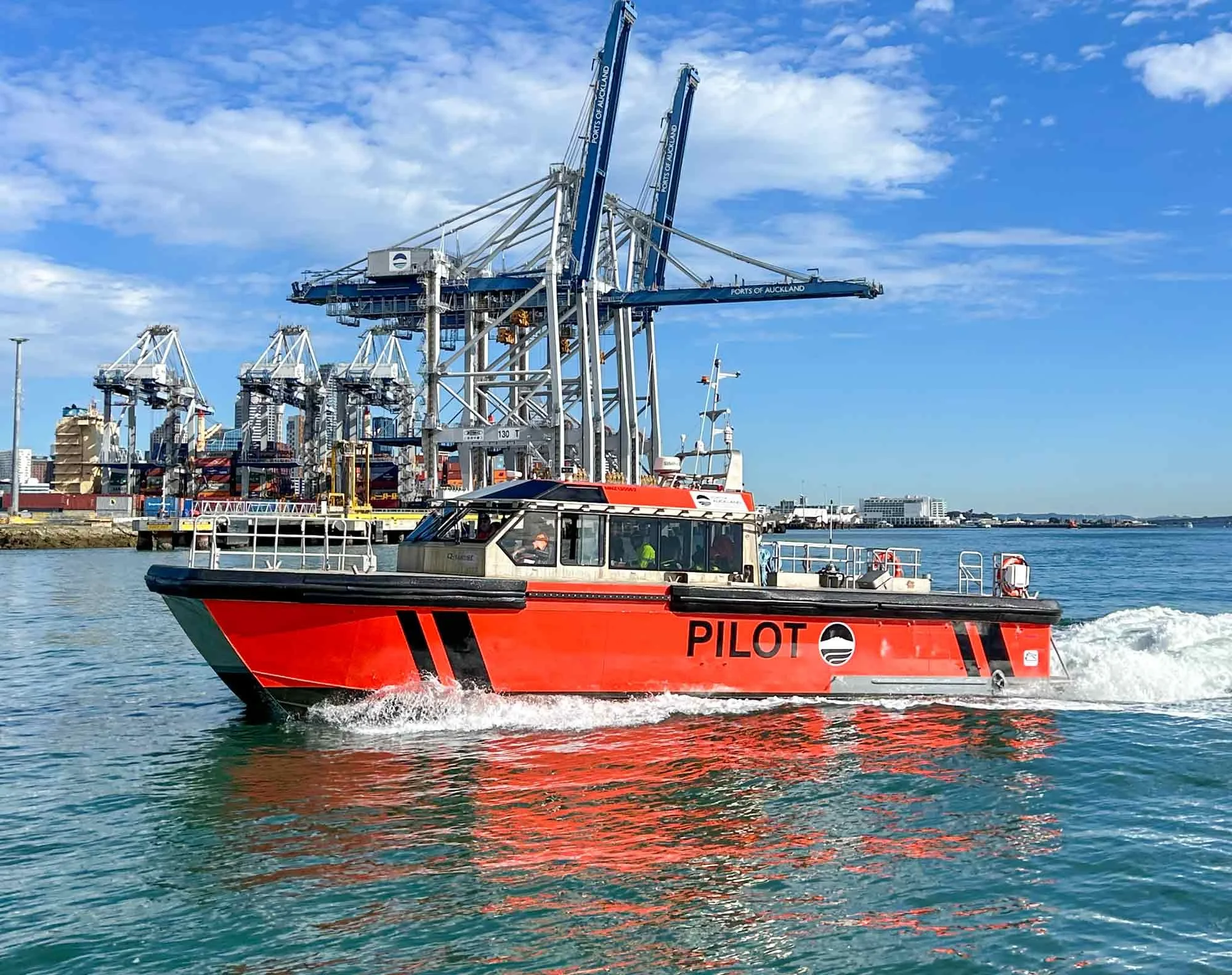A red pilot boat speeding through the water near a port.
