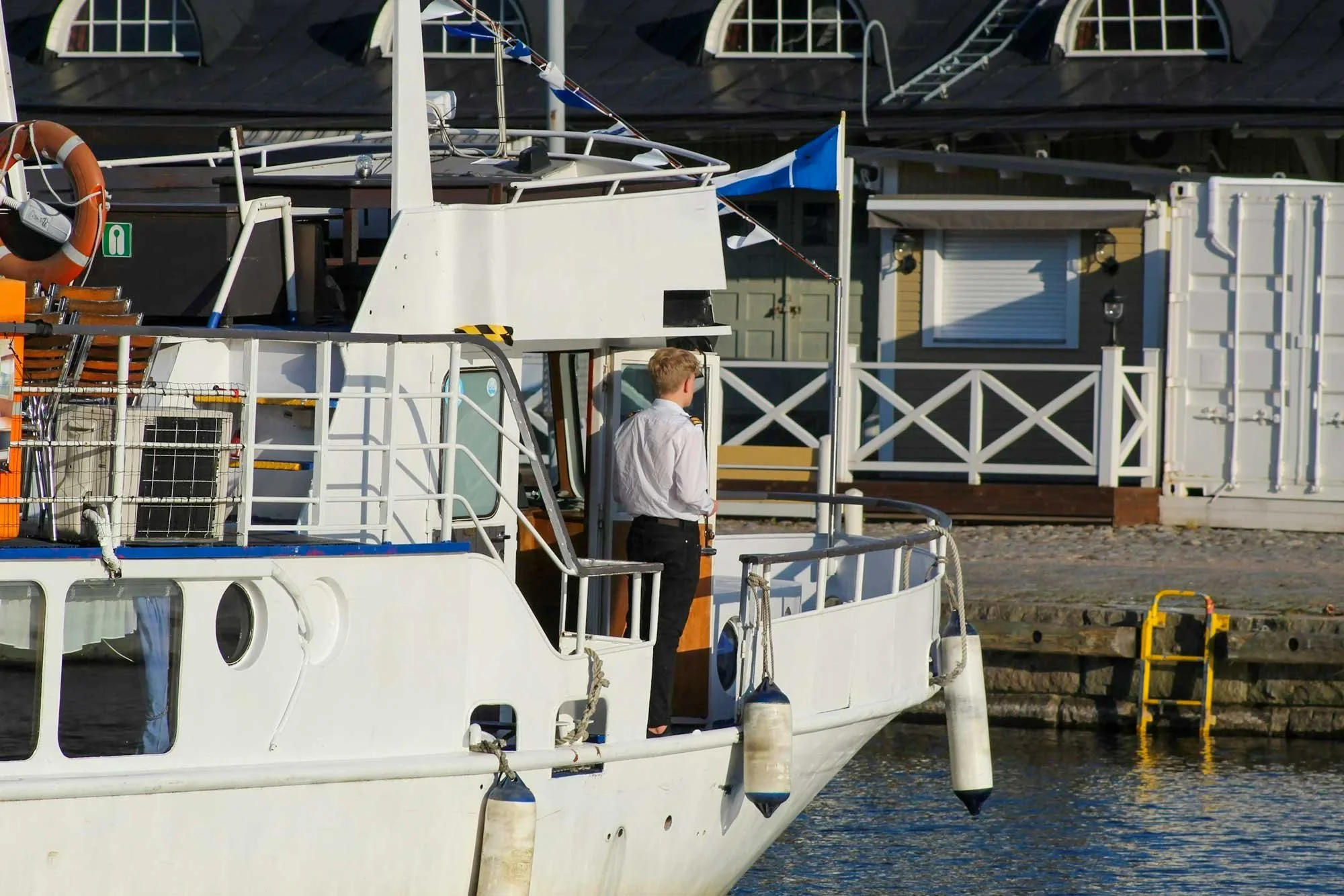 A skipper standing on the deck of a boat docked at a harbour.